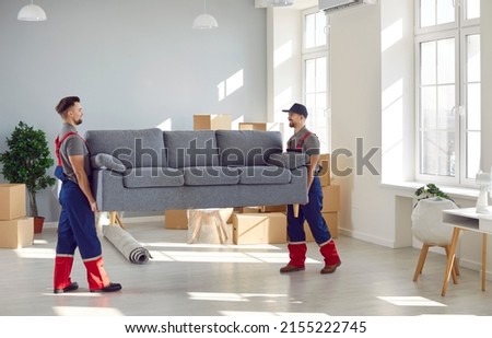Loading service. Male loaders take sofa out of apartment while fulfilling order at moving service. Two young and strong men in overalls carry furniture. Delivery and relocation service concept.
