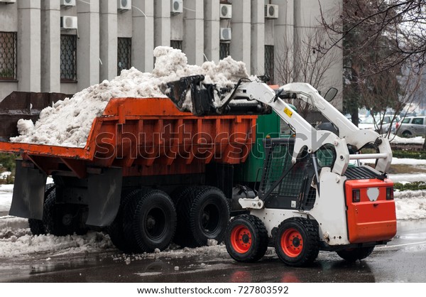 loading snow\
into a truck on a city street in\
winter