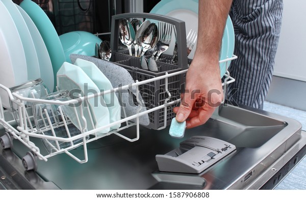 Loading the tablet into\
the dishwasher. A man puts the tablet in the dishwasher to wash\
dirty dishes.