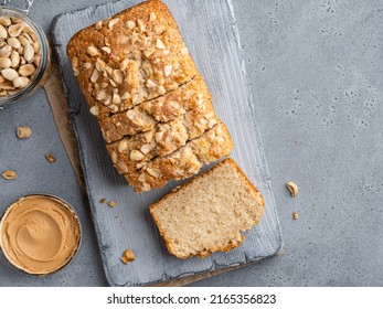 Loaf cake sliced on grey wooden cutting board. Homemade cake made of peanut butter, peanut flour and cinnamon decorated with chopped nuts. Top view. Copy space, gray concrete background. - Shutterstock ID 2165356823