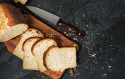 Loaf Of Fresh Sliced White Bread Laid Out On A Cutting Board And A Sharp Knife Nearby. Top View With Copy Space, Bread Crumbs On Black Table Top