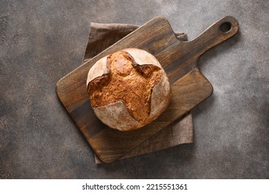 Loaf of freshly baked whole grain bread on cutting board on brown background. Top view.