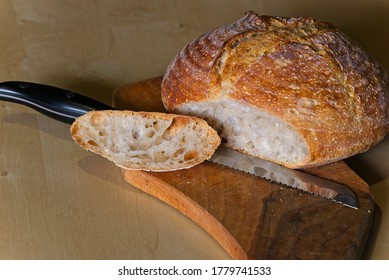 Loaf Of Home Made Craft Bread On Wooden Plate With Sliced Heel And Long Knife.