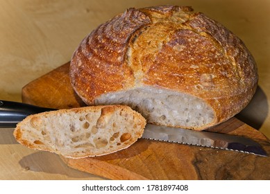 Loaf Of Home Made Craft Bread On Wooden Plate With Sliced Heel And Long Knife.