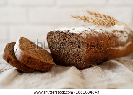 a loaf of home-made dark fragrant fresh bread with sliced slices on a wooden Board against a white brick wall with wheat ears. The concept of rustic home baking.