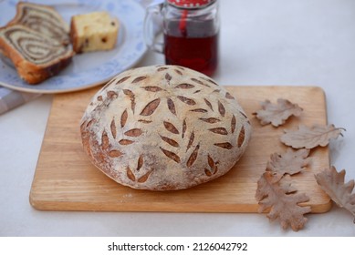 Loaf Of Mixed Wheat Bread With Corn Flour, Sesame, And Flax Seeds On Wooden Board. Home Baked Crusty Corn Bread With Glass Of Raspberry Juice, Slices Of Walnut Roll And Cheese Cake In Background.