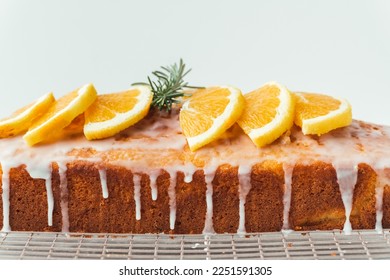 Pan de naranja cubierto con un cristal de confitería con zumo de limón y decorado con rodajas de naranja. Pastel de chile en una parrilla pastelera al lado de una taza de té. Fondo blanco