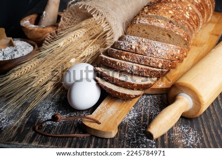 loaf of rye bread, ears of wheat, eggs and a bowl of flour. Close-up.