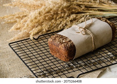 A loaf of sourdough rye bread wrapped in craft paper. Fresh bread is cooled on a special metal wire rack.