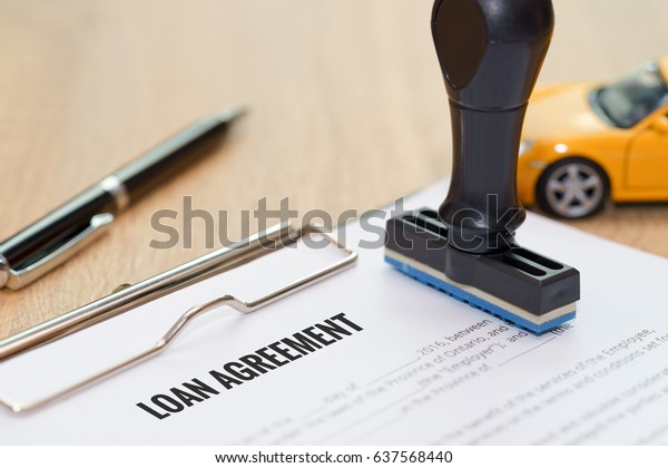 Loan agreement document with rubber stamp and car\
model toy on wooden desk
