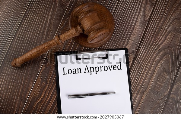 LOAN APPROVED text on the paper with gavel on\
the wooden background
