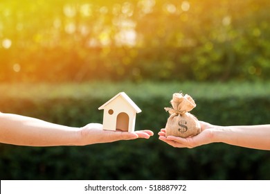 Loans for real estate concept, a man and a women hand holding a money bag and  a model home put together in the public park. - Shutterstock ID 518887972