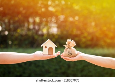 Loans For Real Estate Concept, A Man And A Women Hand Holding A Money Bag And  A Model Home Put Together In The Public Park.