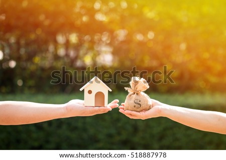 Loans for real estate concept, a man and a women hand holding a money bag and  a model home put together in the public park.
