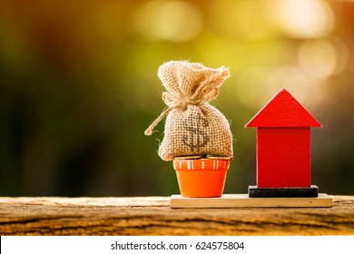 Loans For Real Estate Concept, A Money Bag And A Red Home Model Put On The Wooden In The Public Park.