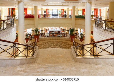 Lobby Of A Grand Hotel With A Staircase And A Restaurant.