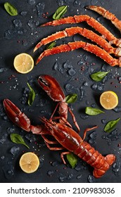 Lobster and crab legs with ice and lemon on dark background top view. Delicatessen crab and lobster seafood on black slate table. Crustacean seafood aesthetics. Luxury food - alive lobster and crab