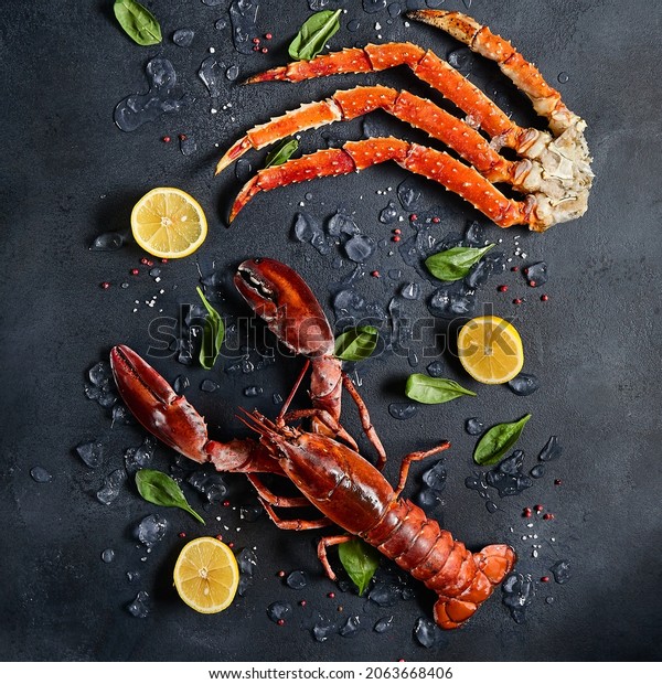 Lobster and crab legs with ice and lemon on dark\
background top view. Delicatessen crab and lobster seafood on black\
slate table. Crustacean seafood. Luxury food - alive lobster and\
crab legs