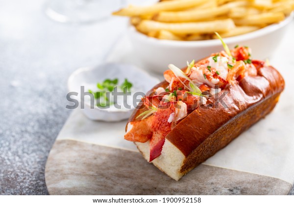 Lobster roll on a brioche bun with fries on a\
marble board
