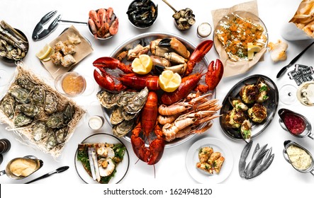 Lobster and seafood party table with oyster, crab, clams, shrimps and crayfish on white tablecloth photographed from above