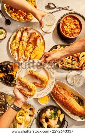Lobster and seafood party table with oyster, crab, clams, shrimps, and crayfish on bright board photographed top view. Set of dishes on the table. On a wooden background, friends sharing food together