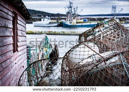 Lobster traps and crab traps stacked on a dock next to a tackle shed with fishing trawlers at background at Whiteway Newfoundland Canada.
