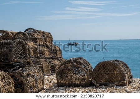 lobster traps on the beach with a fishing boat in the sea in the background in Selsey West Sussex England