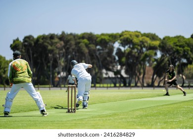 a local cricket match being played on a green cricket oval in summer in australia. australian cricketer batting and bowling in a game in summer - Powered by Shutterstock