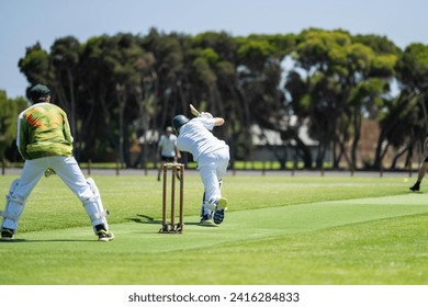 a local cricket match being played on a green cricket oval in summer in australia. australian cricketer batting and bowling in a game in summer - Powered by Shutterstock