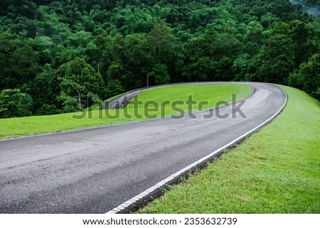 Local curved road on hill slope inside tropical rainforest, the wayside is decorated by green grass.