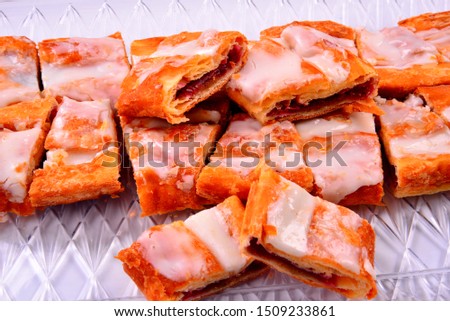 A local Danish pastry treat the Kringle is cut into single serve sizes and laid out on a clear try with a white background. The raspberry Kringle is glazed with icing for that sweet Racine Wi treat. 