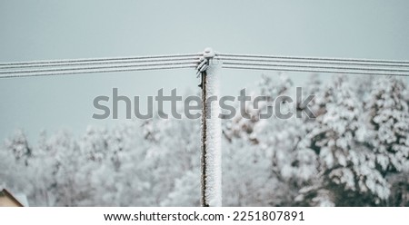 Local electric pole covered with ice and snow. Concept of electricty and blackouts problem during winter snowstroms in rural areas.