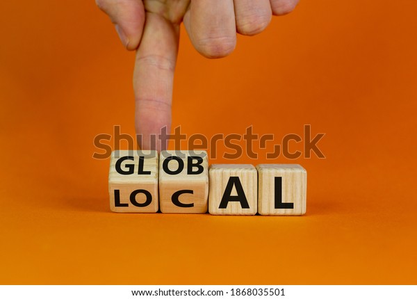 Local or global symbol. Hand turns cubes and changes the word 'local' to 'global'. Beautiful orange background. Business and local or global concept. Copy space.