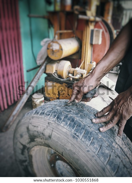 Local recap tire shop : Hands of\
mechanic recap tire car with a needle hole, The old equipment,\
machine for removing rubber from the wheel disc in background\
