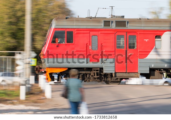 A local train of Russian Railways\
rushes past people standing at the railway\
crossing.