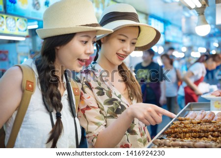 Local vendor sell barbecue grill indoor phuket weekend market Thailand. two asian girl travelers point choosing tasty street food together with hungry smiling face. tourists buying delicious snack.