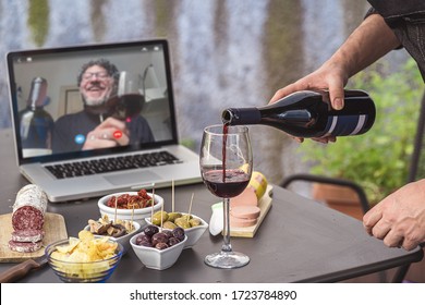 Lockdown aperitif video call party. Adult men are making a pre-meal aperitif with snacks, wine, and Italian appetizers together at home using teleconference platform apps during COVID-19 restrictions