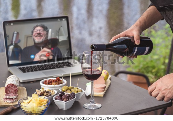 Lockdown aperitif video call party. Adult\
men are making a pre-meal aperitif with snacks, wine, and Italian\
appetizers together at home using teleconference platform apps\
during COVID-19\
restrictions