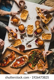 Lockdown Family Fast Food Dinner From Delivery Service. Flat-lay Of Friends Or Relatives Hands Having Quarantine Home Party With Burgers, Fries, Sandwiches, Pizza, Beer Over Table Background, Top View