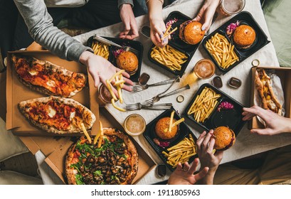 Lockdown fast food dinner from delivery service, getting together. Flat-lay of friends having quarantine party with burgers, french fries, sandwiches, pizza, beer over table background, top view - Powered by Shutterstock