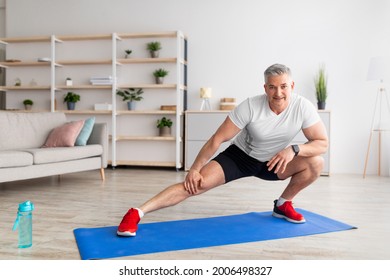 Lockdown home workout. Sporty mature man stretching legs on yoga mat in living room, free space. Active man doing flexibility exercises, keeping fit and healthy, enjoying training - Powered by Shutterstock