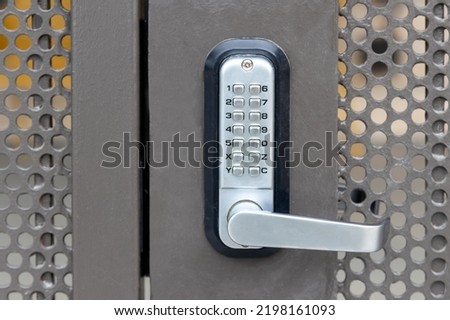 Locked private metal security gate door with push button combination lock system keypad with metallic silver doorknob handle.