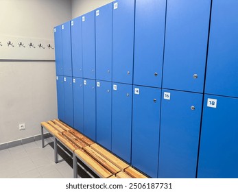 A locker room with blue lockers, wooden bench, and wall hooks on a gray wall for hanging clothes. - Powered by Shutterstock