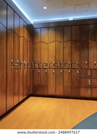 Locker room interior, featuring a row of wooden lockers with wicker fronts. Each locker is labeled with a number, and there are clean, neatly folded white towels stacked on open shelves to the right.