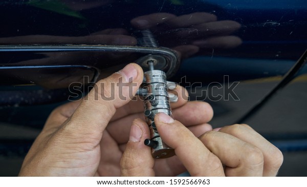Locksmith opening with the lockpicker a blue car\
that its owner has lost the\
keys