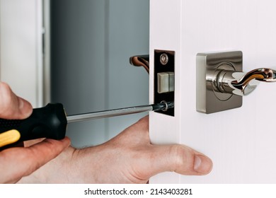 A locksmith repair the door lock in the room. A locksmith fixing lock with yellow screwdriver. Close-up of repairing door. Selective focus