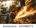 Locksmith in special clothes and goggles works in production. Metal processing with angle grinder. Sparks in metalworking.