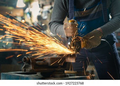 Locksmith in special clothes and goggles works in production. Metal processing with angle grinder. Sparks in metalworking. - Shutterstock ID 1927223768