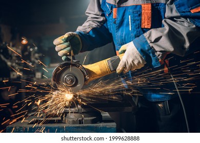 Locksmith in special clothes and goggles works in production. Metal processing with angle grinder. Sparks in metalworking