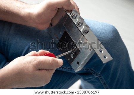 The locksmith using a screwdriver to adjust a metal door lock mechanism, demonstrating a close-up of the locksmithing process and repair work with attention to detail